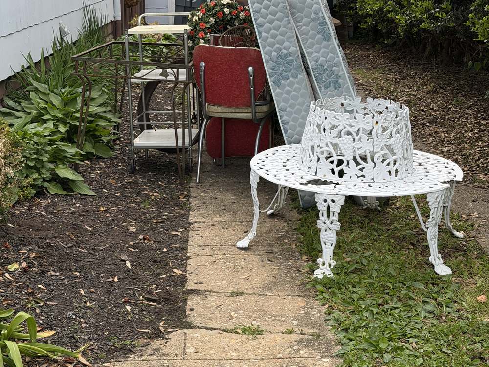 Mattresses, a vintage chair, and metal furniture staged along a side walkway before junk removal in Annapolis, MD