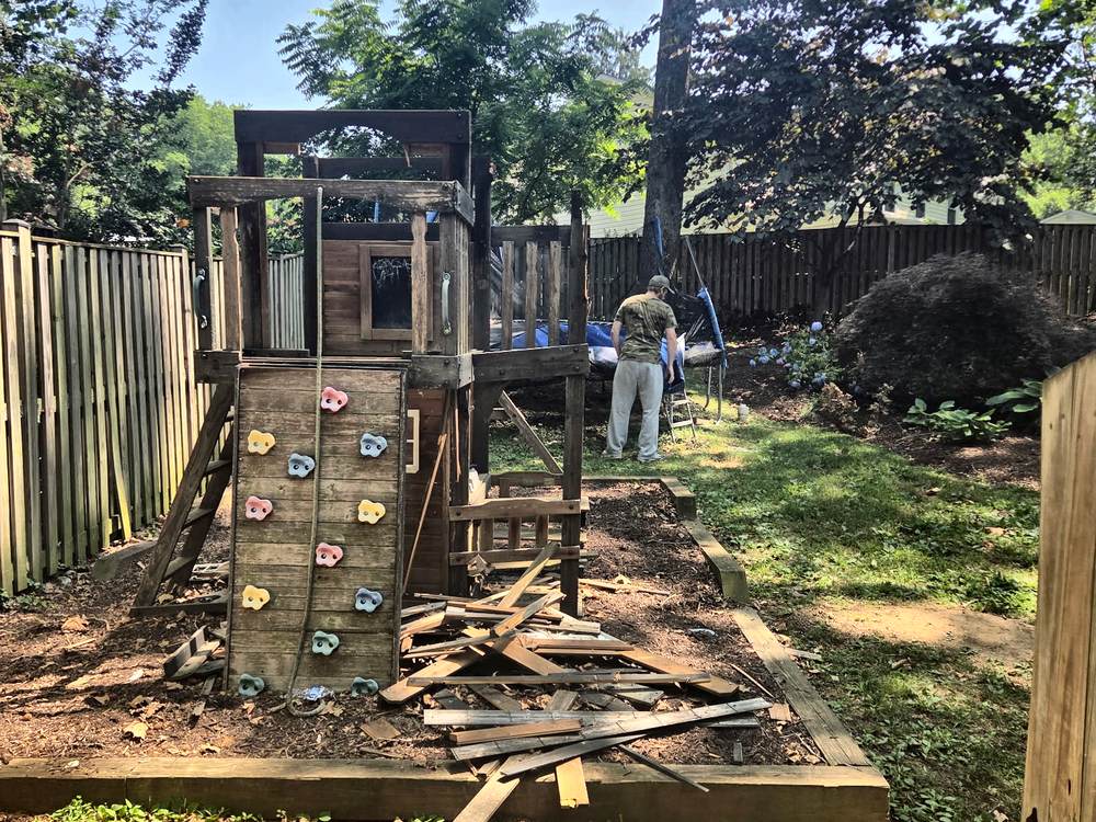 Wooden playset with climbing wall being dismantled in a fenced backyard in Arnold, MD