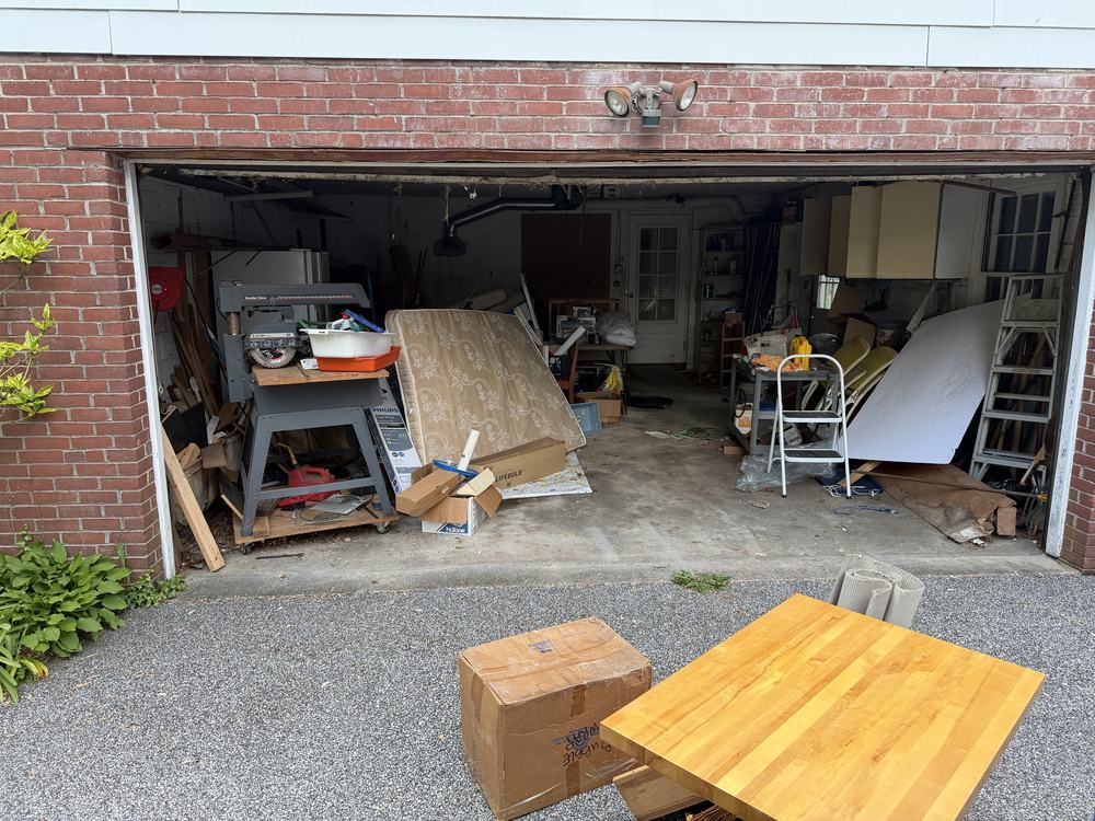 Two-car brick garage crammed with a saw, mattress, boxes and ladders before a garage cleanout in Catonsville, MD