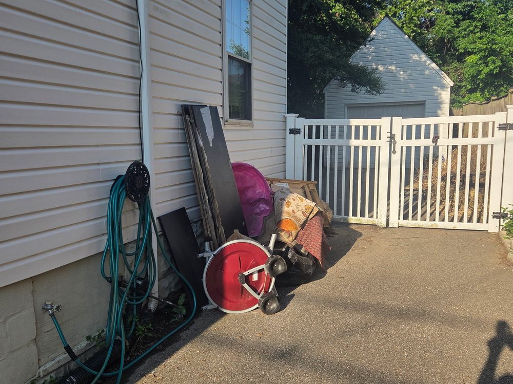 Side-yard pile of a rolled rug, hose reel, boards and trash bags before junk removal in Catonsville, MD