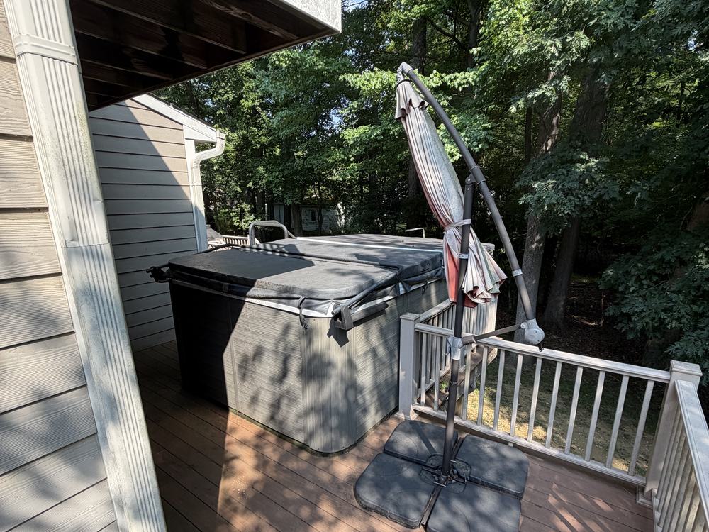 Intact swim spa with cover and cantilever umbrella on a wooded backyard deck before demolition in Clarksville, MD