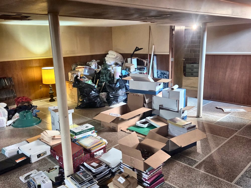 Terrazzo-floored basement covered in boxes, papers and bins before an estate cleanout on Oakland Mills Road, Columbia, MD