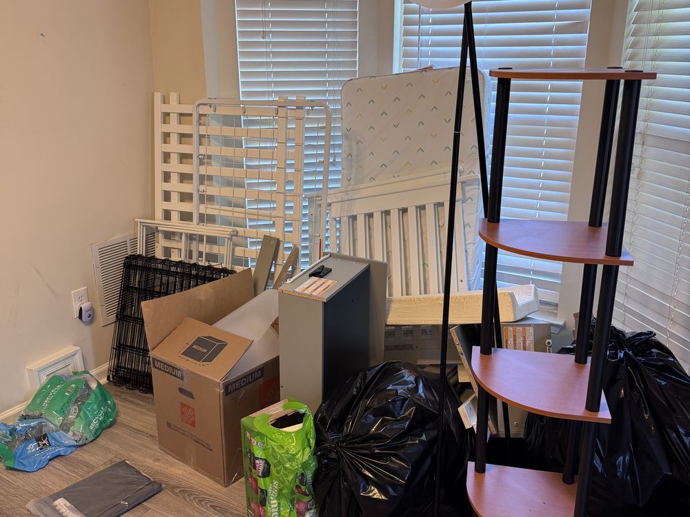 Cluttered room before a tenant turnover cleanout with a crib, shelving, boxes and trash bags in a Walden rental in Crofton, MD