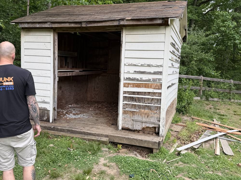 Large weathered clapboard shed with peeling paint before demolition in Davidsonville, MD