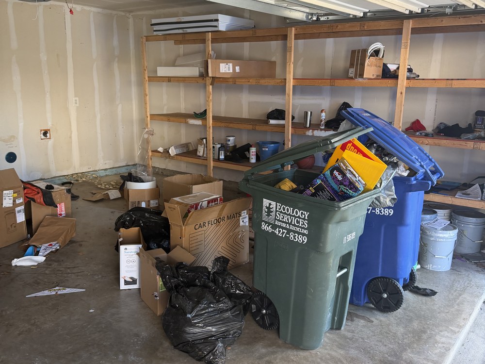 Garage floor cluttered with boxes, bags and recycling carts before a cleanout on Southmoor Street in Elkridge, MD