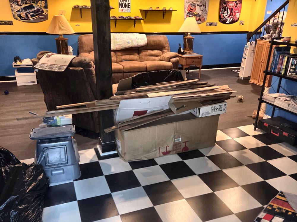 Finished basement with a pile of wood trim, cardboard boxes, and a trash bag before a cleanout in Ferndale, MD