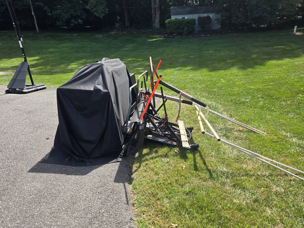 Driveway piled with a trampoline frame, a covered grill, and metal poles before a junk pickup in Fulton, MD