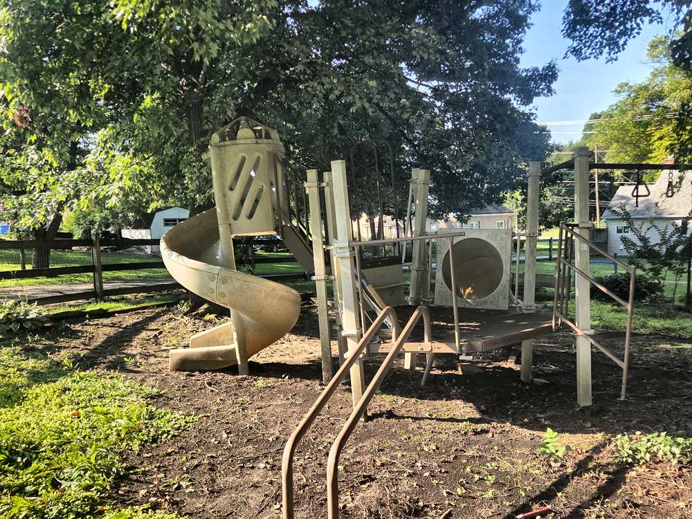 Old commercial-size metal and plastic playground structure with a spiral slide standing in a yard before demolition in Fulton, MD