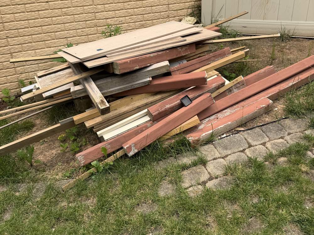 Pile of old deck boards, painted trim and framing scraps stacked against a wall before a lumber pickup on Suffolk Way in Hanover, MD