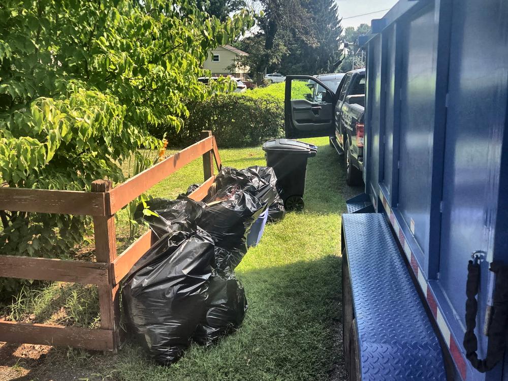 Row of stuffed trash bags along a fence with the MD Junk Pros truck before a trash pickup on Mound Street in Hanover, MD