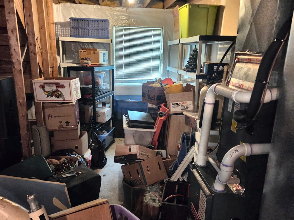 Basement packed with boxes, storage bins, and stored clutter around the furnace before an estate cleanout in Millersville, MD